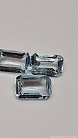 Three rectangular emerald cut natural sky blue topaz gemstones shown on a plain background, displaying clarity and color.