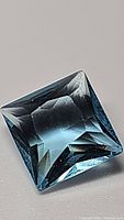Close-up image of the square princess-cut natural Swiss blue topaz gemstone, showing blue color and facet reflections.