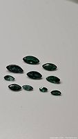 Photo showing 10 deep green marquis cut natural emerald gemstones in two rows on plain background.