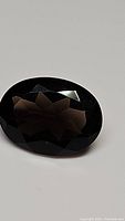 Close-up image of an oval cut natural smokey quartz gemstone showing faceted cuts and deep dark brown color.