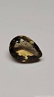 Photo of a single pear-shaped natural citrine gemstone with facets and light golden color visible.
