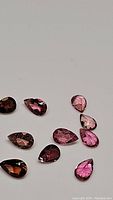 Ten natural bright pink pear cut tourmaline gemstones laid out on a neutral background, showing clarity and faceting details
