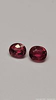 Pair of natural oval cut hot pink tourmaline gemstones shown from top angle on gray surface.