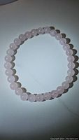 Photo showing round polished soft pink rose quartz beads arranged in a circle to form a stretchy bracelet on a plain surface.