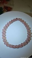 Round baby pink strawberry quartz bead bracelet, stretchy, displayed flat in circular shape on white surface with shadow and light reflection.
