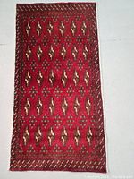 Full view of the rectangular red Turkmen rug with geometric patterns on light floor background.