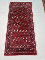 Full view of the rectangular red wool rug with geometric designs and multiple patterned borders.