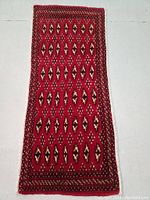 Full view of the rectangular red Turkmen rug showing overall geometric diamond pattern and borders.