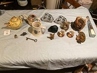Wide view of the lot including teapots, figurines, bookends, key and assorted small decor pieces on cloth surface.