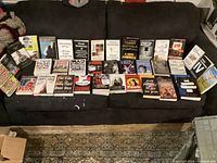 Photo showing an assortment of 34 books arranged on a couch, covering various topics and authors, mostly paperbacks.