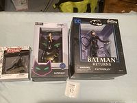 Three Catwoman figurines in original boxes displayed side by side: a small Justice League figurine, a mid-sized DC Catwoman figurine, and a larger Batman Returns DC Gallery figurine.
