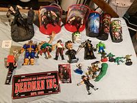 Wide view of assorted collectible figurines, wrestling figures, license plate and collectible cups arranged on table