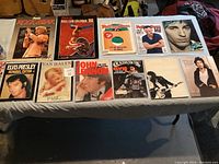 Top down view of 13 collectible rock magazines spread on a table, showing covers of iconic rock and music artists including Elvis Presley, John Lennon, Van Halen, Bruce Springsteen, and Rolling Stone issues.