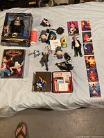 Overview of assorted collectible toys and memorabilia including boxed DC Multiverse figure, Futurama DVD, Marvel card tin and various figures on a bed surface.