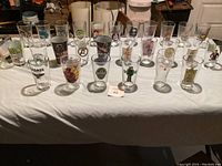 Photo showing 29 assorted collector cups laid out on white tablecloth, featuring various pop culture and beer themes.