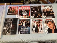 Full view of all ten music magazines laid out on a surface showing covers with various artists such as WWE, Def Leppard, Queen, Metallica, Bruce Springsteen, Eagles, Fleetwood Mac, David Bowie, and Pat Benatar.