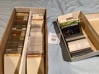 Overhead view of two cardboard boxes containing hockey cards: left box with plastic-sleeved cards and labeled dividers, right shallow box with loose cards.