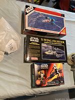 Three unopened Star Wars model kits shown on a bed: an X-Wing Fighter, a Y-Wing Fighter, and an Imperial Speeder Bike with rider.