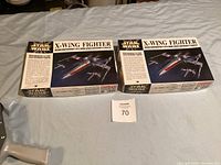Two unopened Star Wars X-Wing Fighter model kit boxes placed side-by-side on a bed.