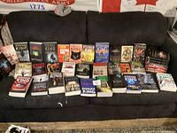 Photo showing a wide view of over 30 Stephen King novels spread across a dark sofa including The Outsider, Pet Sematary, The Dark Tower collection, It, and others.