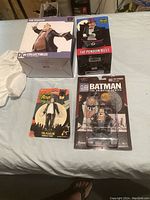 Four collectible Penguin figures in box displayed on a bed, including a large boxed statue, a bust box, a blister card figure, and a LEGO-style figure in packaging.