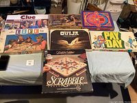 Photo showing seven vintage board game boxes including Clue, Life, Scrabble, Ouija, Payday, and two other classic games.