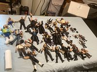 Overview of all 23 wrestling figurines and plush doll laid out on a blue sheet, showing a variety of characters including those in black wrestling gear with tattoos and muscular physiques.