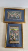 Two framed Indian hand painted paintings with decorative borders and vibrant scenes, showing rural life and figures.