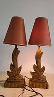 Two vintage Art Deco style table lamps with reddish-brown fabric shades, one slightly stained, shown with cords and bases on neutral surface.