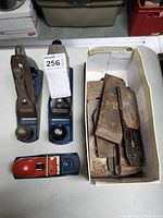 Front angle showing three hand planers and box with extra blades on table.