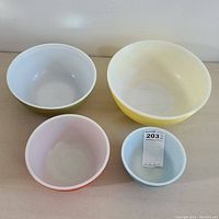Full view of four colorful Pyrex nesting bowls showing yellow, light green, pink, and blue colors with varying sizes.