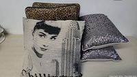 Five pillows together showing various designs: Audrey Hepburn graphic, leopard print, silver sequin, neutral pattern