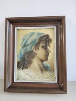 Front view of framed original painting showing a woman in profile wearing a blue headscarf; wooden frame with silver inner border visible.