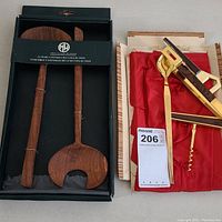 Set of six bar and kitchen utensils. Two wooden Mountain Woods utensils in black packaging; four gold-toned Hart Vergoldet metal utensils with dark brown accents in a fabric-lined wooden box with red lining.