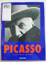 Front cover of the Picasso coffee table book by Taschen, showing a black-and-white photo of Picasso and bold orange text on a blue background.