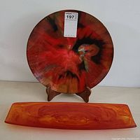 Round Seetusee glass plate with red and black swirls on wooden stand, with visible wear on back