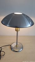 Side view of the UFO style table lamp showing the metallic dome shade and circular base with power cord.