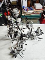 Oblique angle showing top and side of metal chandelier with leaves and crystal drops.