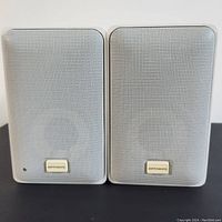 Front view of two white vintage metal speakers with perforated grills and Optimus badge