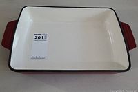 Top view of rectangular cast iron pot showing white enamel interior with black rim and red handles, labeled with MaxSold lot number sticker