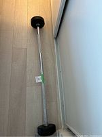 Full length side view of the 30 lb barbell on a wooden floor against a wall.