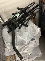 Angled view of the black powder-coated steel bike rack showing the platform and hooks, placed on plastic bags inside a metal storage cage.