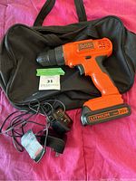 Black & Decker cordless drill, battery charger, and carry bag on a red surface.