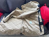 Brown quilted protective cover laid out on a couch showing its quilted texture and black clips for attachment.