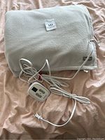 Light gray electric blanket folded with attached digital control panel and power cord laid out on a bed.