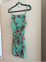 Front view of teal floral cocktail dress with beaded straps hanging on hanger.