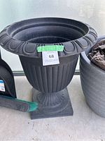 Front-side view of the large black planter pot showing fluted sides, ornate wide rim, and pedestal base.