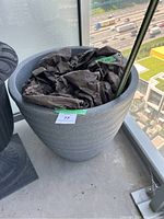 Photo of a large grey plastic pot with black paper inside, placed on a balcony with a city view in the background.