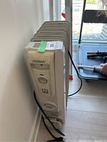 Front view of the Noma portable heater showing control panel with rotary dial, power switch, brand name, and power cord extending downwards.