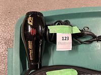Black Parlux 3800 Eco Friendly blow dryer with its power cord coiled on top of a green container, showing side branding and control settings.